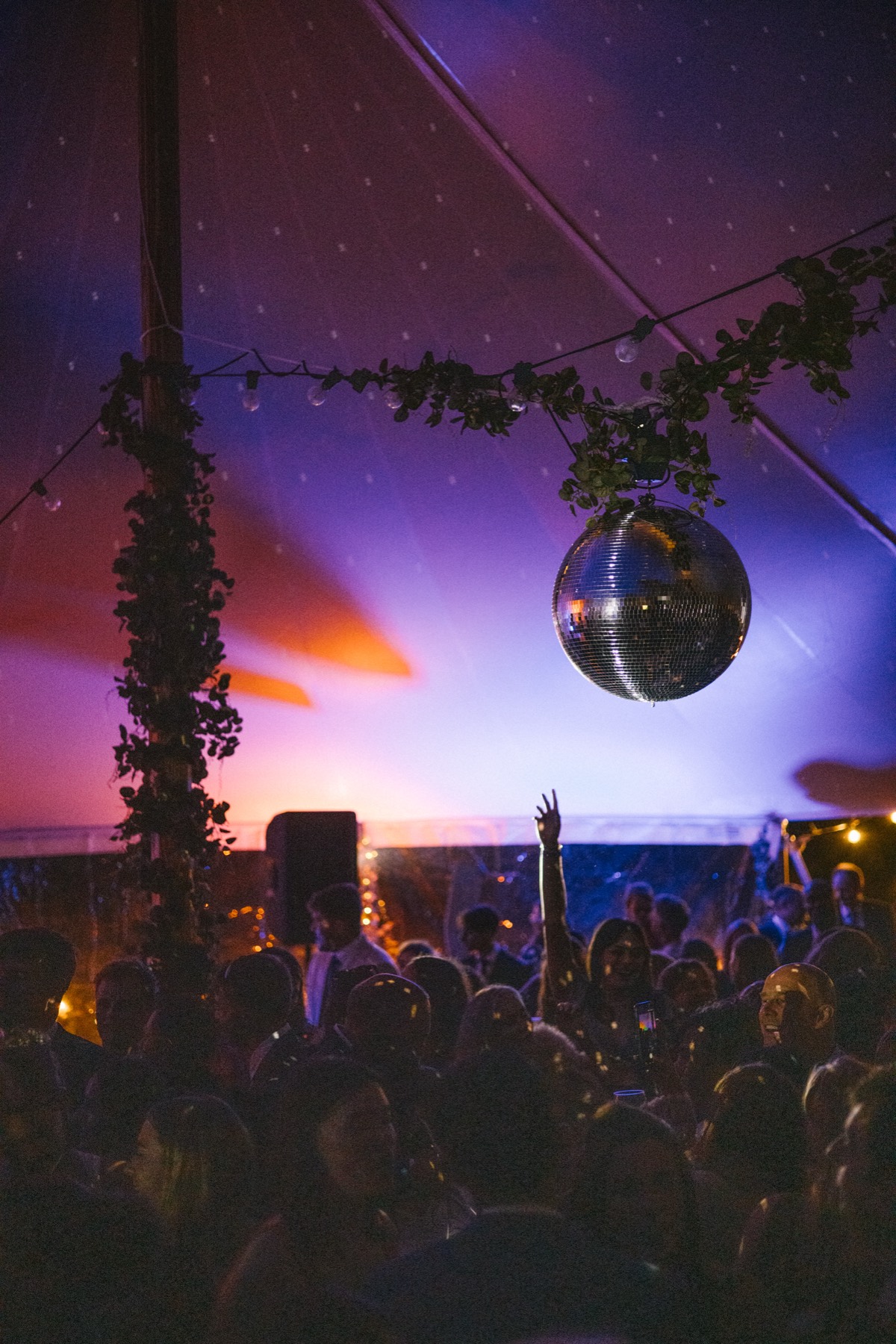 Wedding guests dancing with hands in the air beneath a disco ball