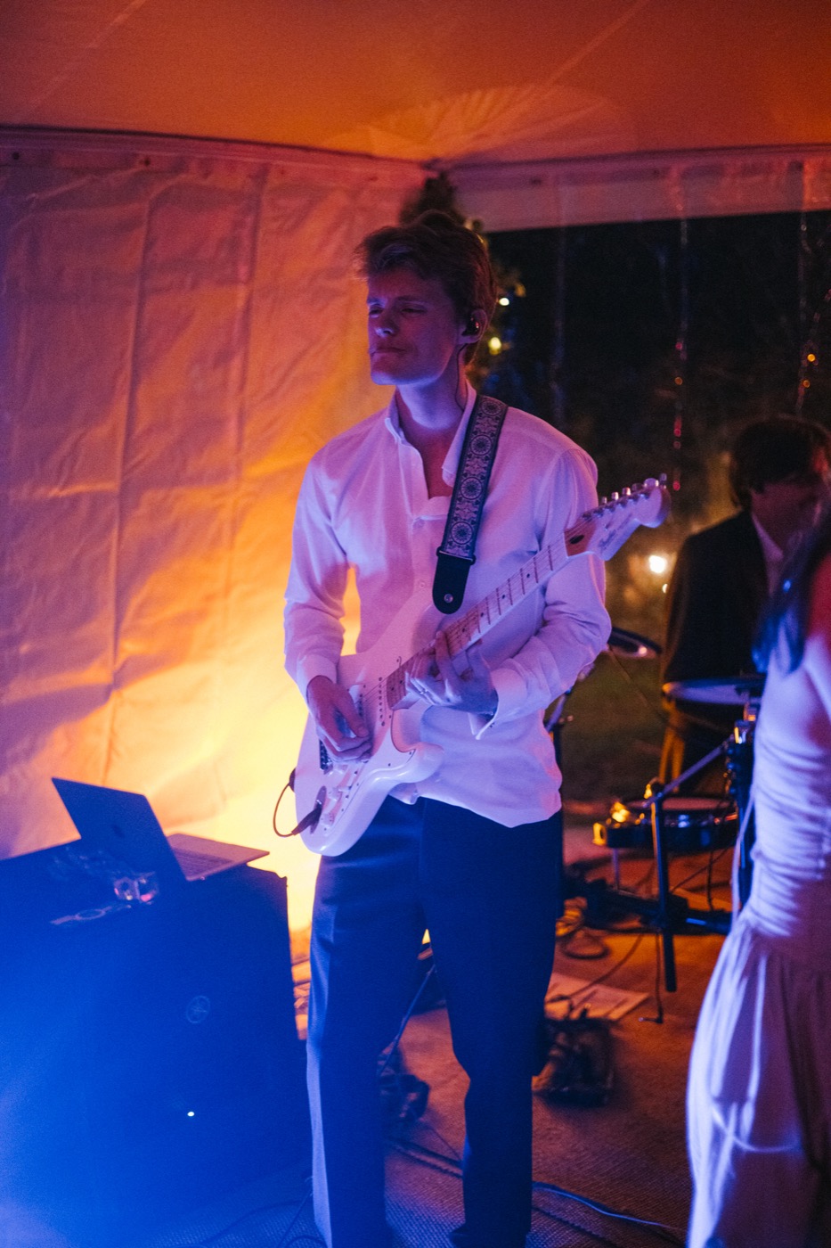 Josh playing a white electric guitar under orange stage light